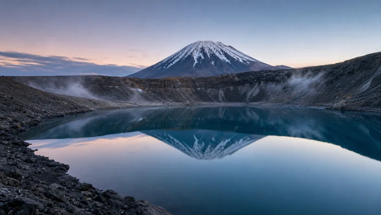 A snow-capped mountain mirrored in a still lake at dusk